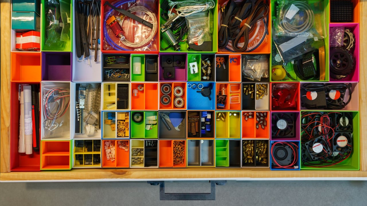 Top view of a neatly organized drawer filled with colorful containers holding various tools and electronic parts.