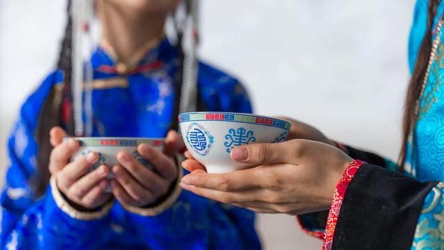 Close-up of people in traditional attire holding decorative tea cups during a ceremony indoors.