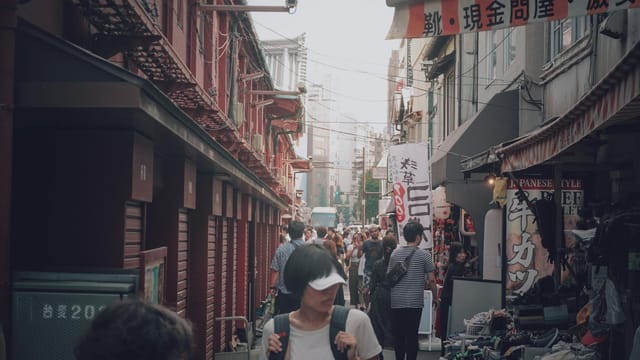 A bustling city street market filled with people shopping at vibrant stalls under warm daylight.