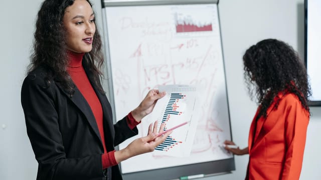 Women presenting business data during a corporate meeting with charts.