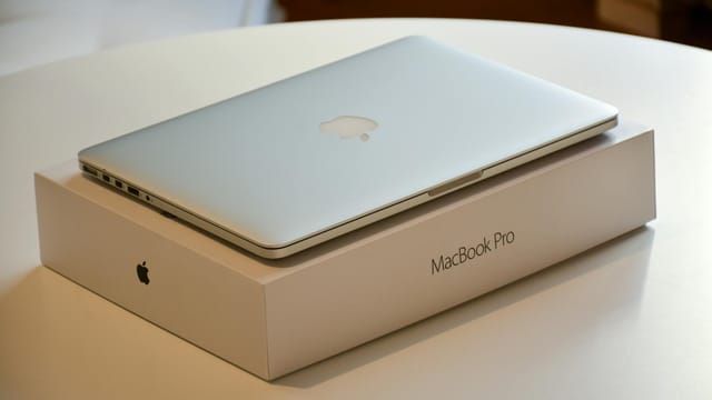 A MacBook Pro laptop placed on its original packaging on a white indoor table.