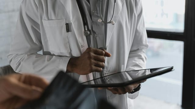A professional medical practitioner holding a tablet, focused on work in a clinical setting.