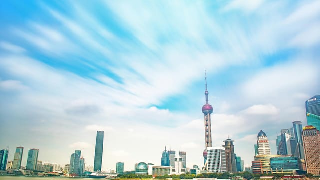 Vibrant Shanghai skyline featuring the iconic Oriental Pearl Tower under a bright blue sky.