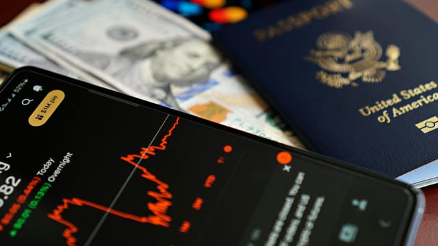Close-up of smartphone with stock chart, cash, and US passport, symbolizing travel and finance.