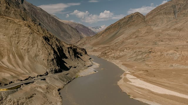 Scenery view of narrow roadway between high rough mountains under blue cloudy sky in daytime
