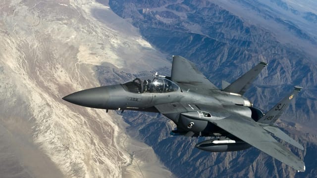 A military fighter jet flying above rugged mountain ranges, showcasing advanced aviation technology.