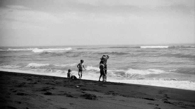 Black and white photo of children playing on a Kamchatka beach with waves in the background.