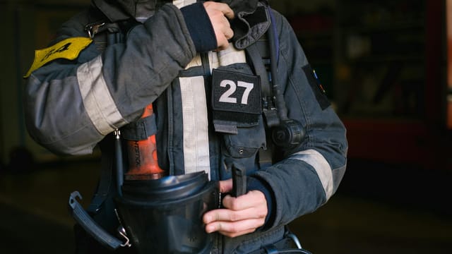 Firefighter adjusting gear in protective uniform, showcasing firefighter number 27 patch.