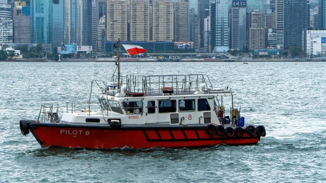 Pilot boat cruising on Victoria Harbour with Hong Kong skyline background.