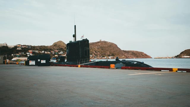 A submarine docked at a pier, surrounded by picturesque hills and calm waters.