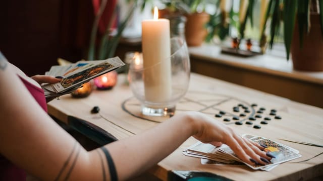 Crop unrecognizable fortune teller predicting fate with tarot cards near shiny candle at home