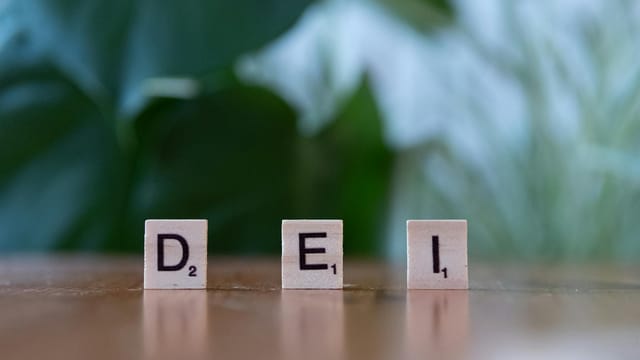 Wooden letter tiles spelling 'DEI' on a table symbolizing diversity, equity, and inclusion.