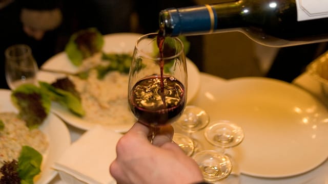 Close-up of red wine being poured into a glass at an elegant dinner with lush salads on the table.