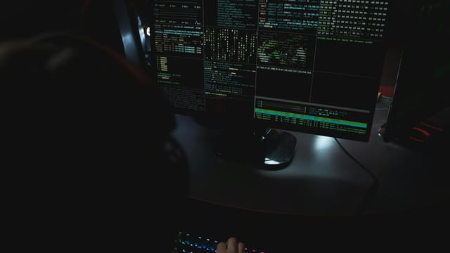 Dark room setup with code displayed on PC monitors highlighting cybersecurity themes.