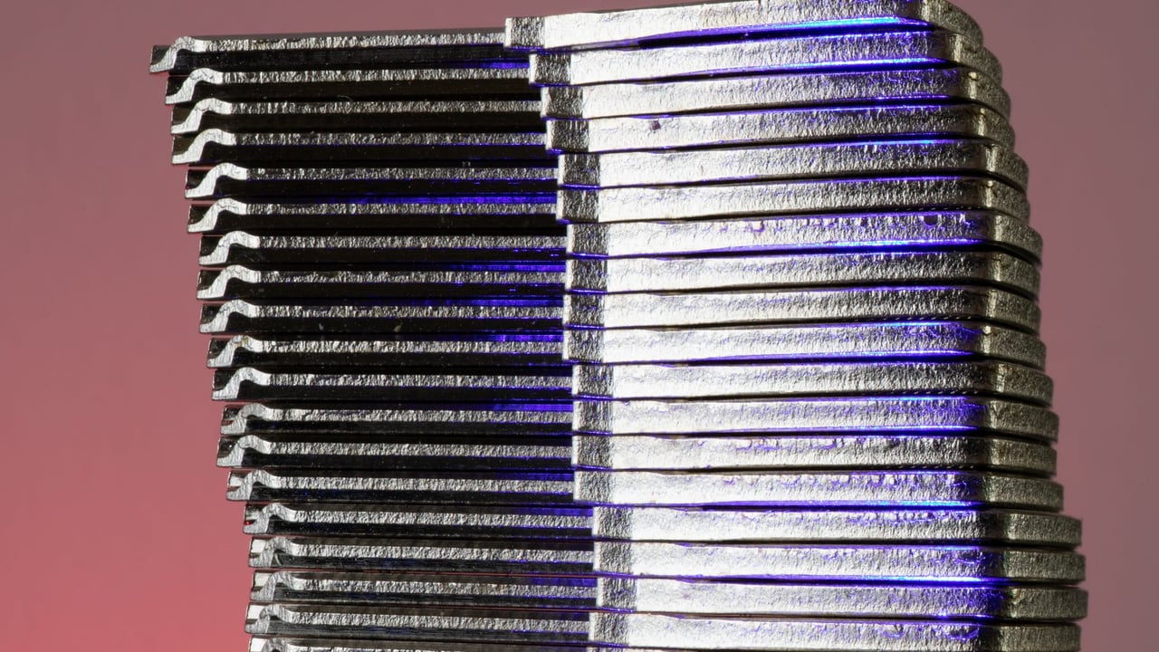 Close-up of stacked metallic sheets reflecting purple light against a gradient background.