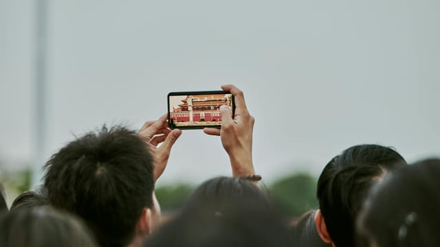 Tourists photograph historical landmark using a smartphone at an outdoor event.