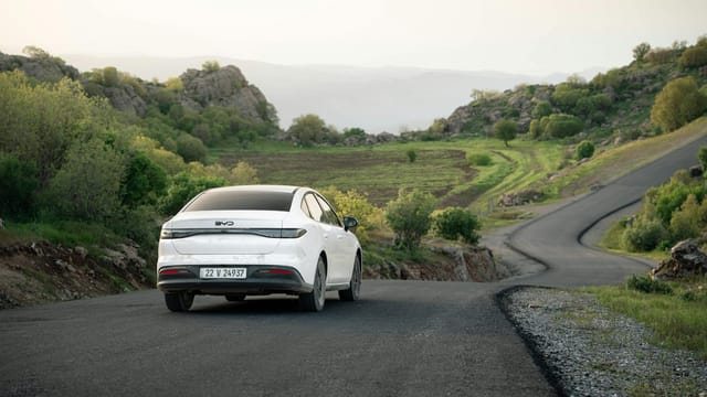 A white car drives on a winding road through scenic hills in Shaqlawa, Iraq during daylight.