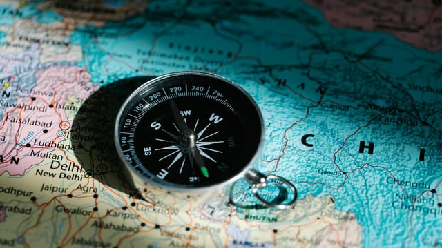 A compass resting on a map of China and India signifies exploration and adventure.