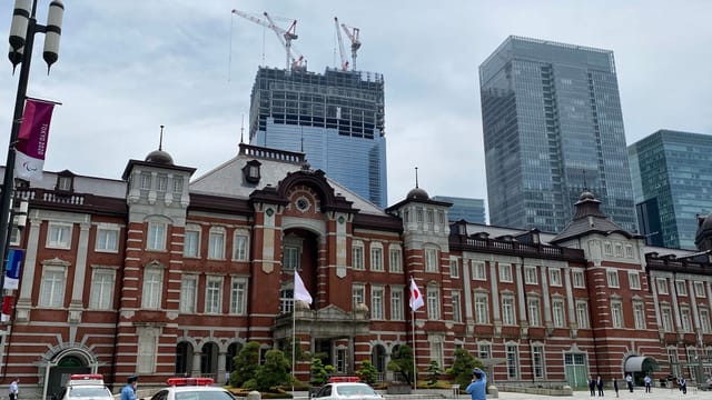 Tokyo Station's iconic facade with police cars and officers as skyscrapers loom in the background.