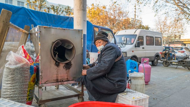 Elderly man wearing a face mask beside a market stall in Nantong, showcasing urban life.