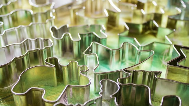 Close-up of diverse metal cookie cutters in abstract shapes on a colorful surface.