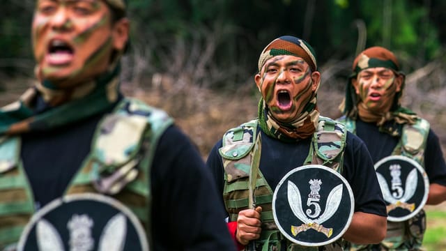 Military soldiers shouting commands in camouflage uniforms during an outdoor training drill.