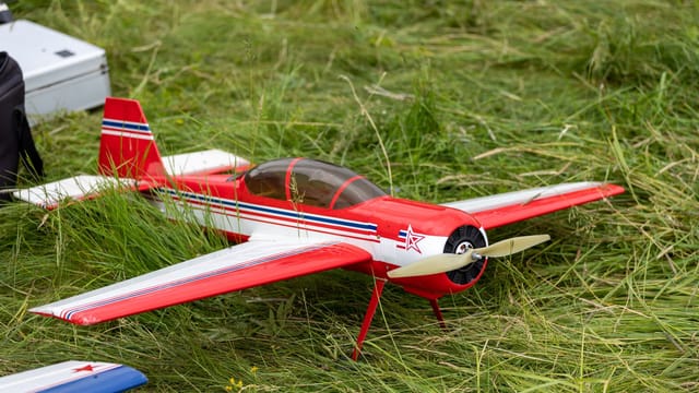A vibrant red model airplane with propeller on grass, showcasing aviation hobby.