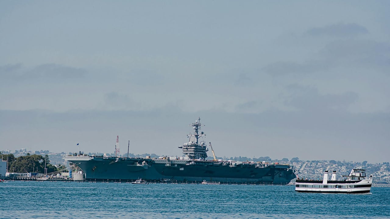 USS Carl Vinson aircraft carrier docked in San Diego harbor with a ferry in view.