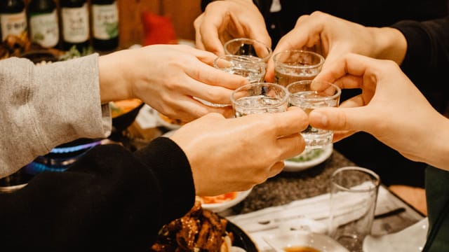 Close-up of friends clinking soju shot glasses in a lively indoor celebration.