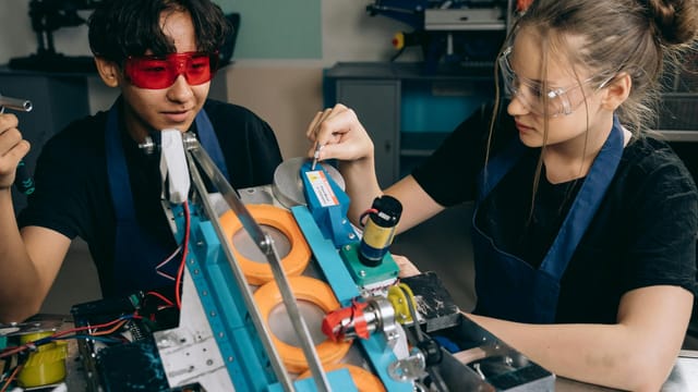 Two students collaborating on a robotics project in a tech lab, focusing on machinery details.