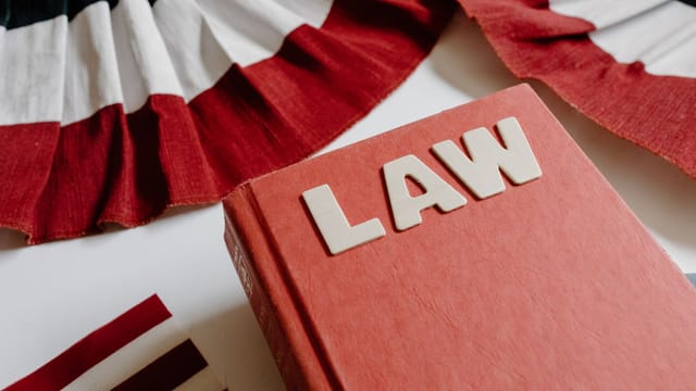 A law book with bold letters placed beside a red, white, and black decorative ribbon.