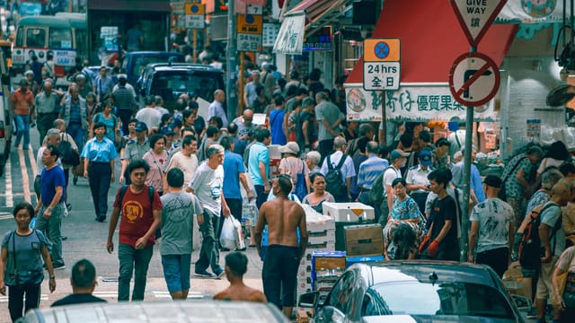 A lively street market in Hong Kong bustling with people, shops, and vehicles during the day.