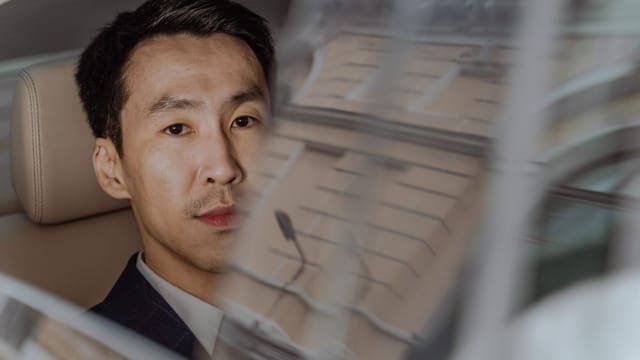 Asian businessman in a suit gazes through a car window showing city reflections.