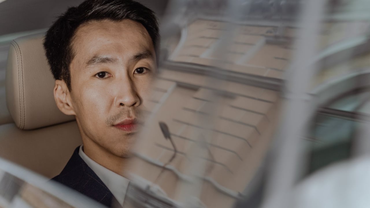 Asian businessman in a suit gazes through a car window showing city reflections.
