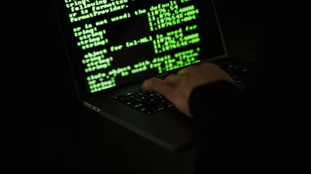 Crop unrecognizable computer geek typing on netbook with codes on screen while hacking system in darkness