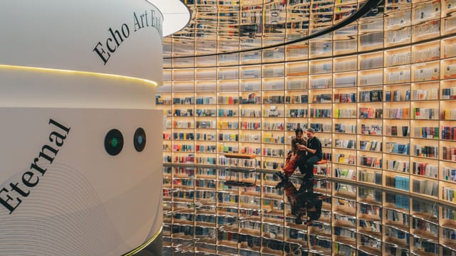 Contemporary library in Shenzhen featuring reflective floors and people observing an art exhibition.