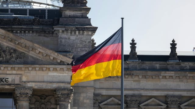 German flag waves at the iconic Reichstag building in Berlin, symbolizing national pride.