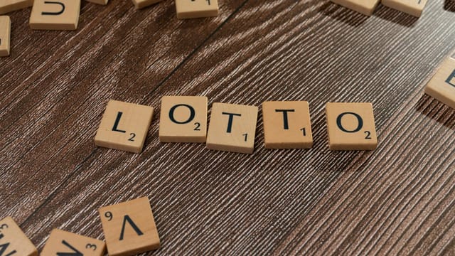 Scrabble tiles spelling 'LOTTO' on a wooden table surface, symbolizing chance and gaming.