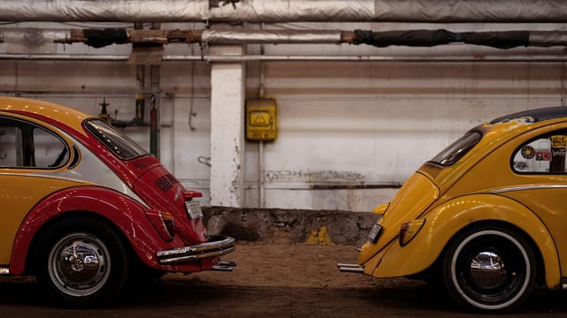 Two vintage Volkswagen Beetle cars in an industrial indoor environment.