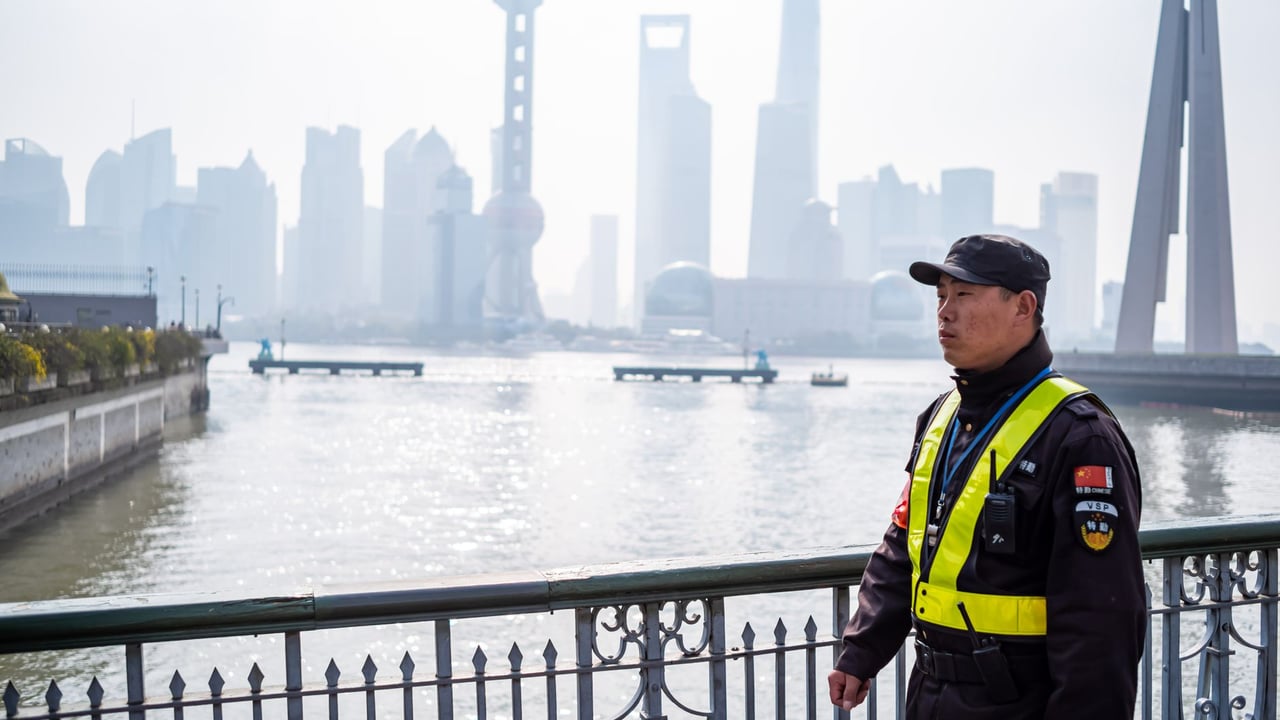A police officer in uniform on a bridge with Shanghai urban skyline and river background.