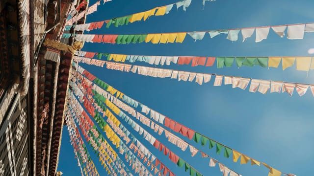 Vibrant prayer flags adorn a monastery under a clear blue sky, depicting a serene cultural scene.