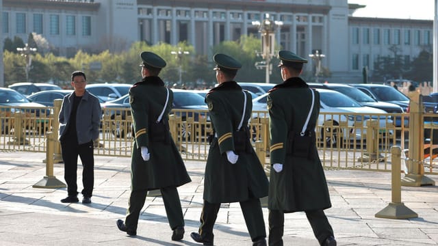 Uniformed guards march in formation outside a grand museum building on a sunny day.
