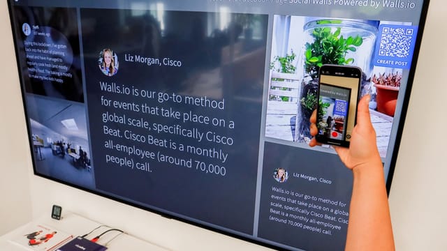 A person uses a smartphone to scan a QR code displayed on a large screen indoors.