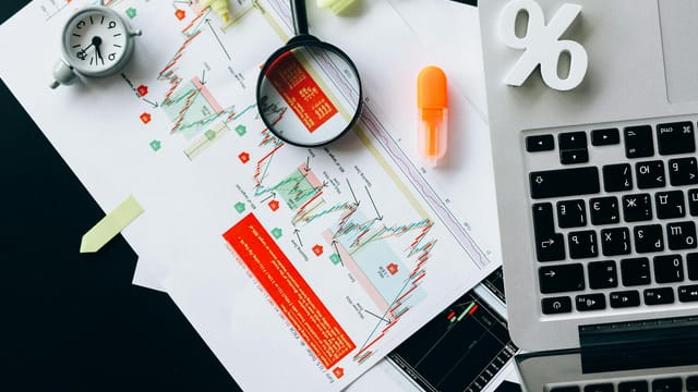 Top view of financial documents, charts, and laptop organized on a desk.