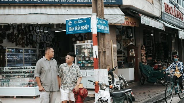 Two men talking beside motorbikes in a vibrant market street, showcasing local street life.