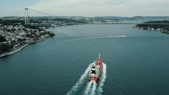 Aerial view of a cargo ship navigating the Bosphorus in Istanbul, Türkiye, beneath a large bridge.