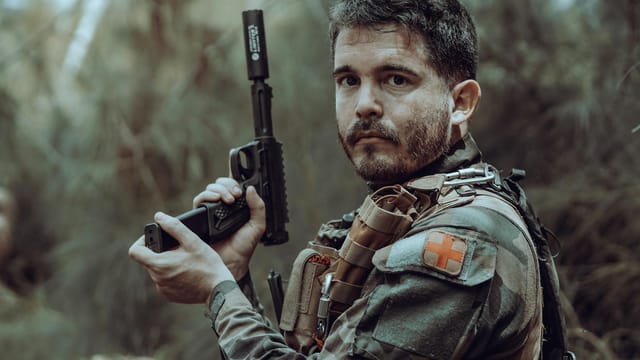 A soldier in tactical gear holds a weapon in a dense jungle environment, ready for action.