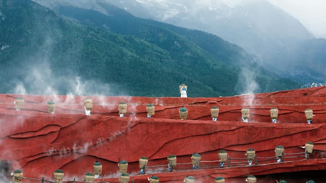 Cultural performance with people in red landscape against mountain backdrop.