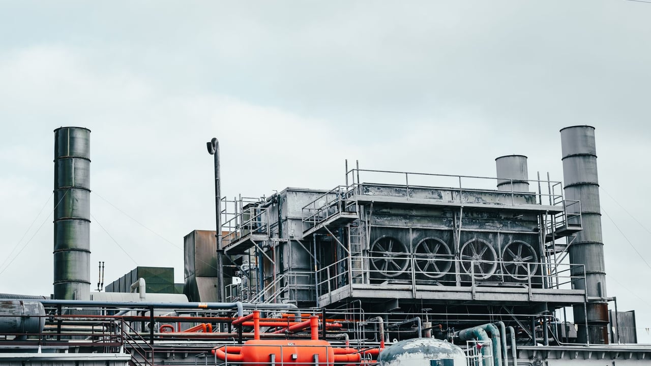 Illustrative image: Industrial factory with metal pipes and special equipment surrounded with fences located against cloudy sky on street with power lines in town