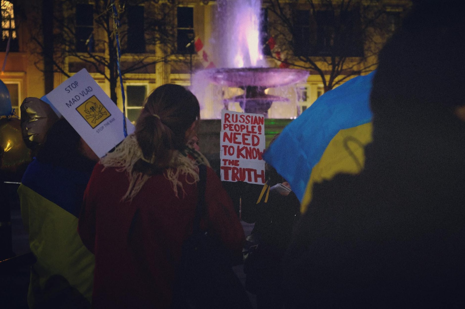 Protesters in London rally against war, holding placards under city lights, expressing solidarity with Ukraine.